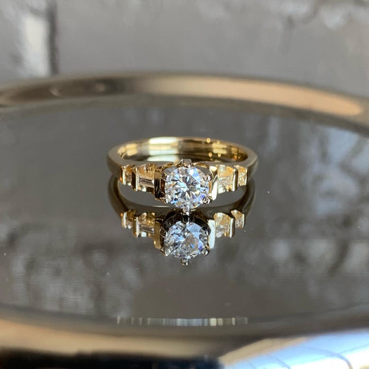 A sparkly diamond ring sits on top of a mirrored surface.
