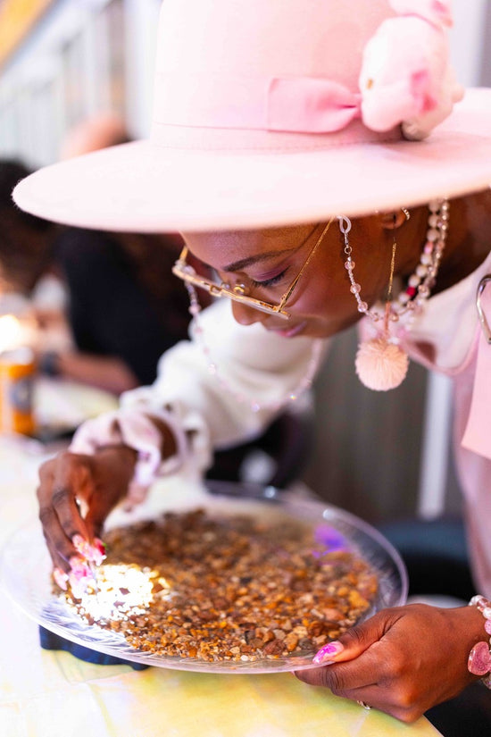Mining guest in a pink hat and glasses leans over a light box and clear tray, picking through gravel with tweezers searching for Montana sapphires. 