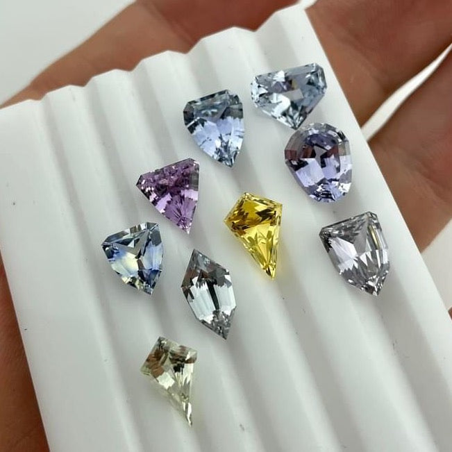 A tray of uniquely cut natural sapphires from Sri Lanka are offered as a selection for our customer to choose from.  The colors are greys, yellow, purples and teals and the shapes are unique sheild, hexagon, and mixed kite cuts.