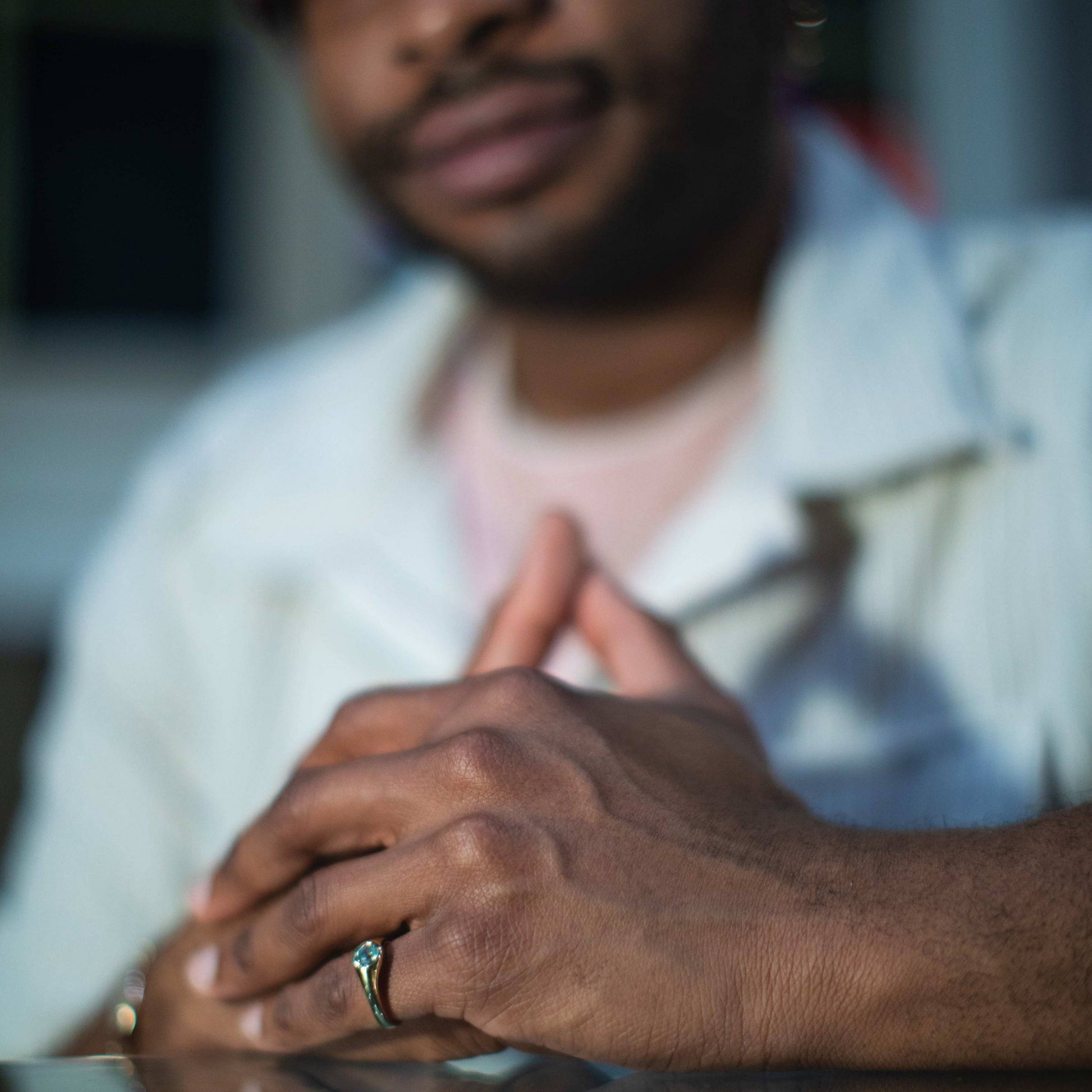 Tyler has this ring on his pinky finger and is sitting with his hands clasped which are in focus.  Our of focus is his torso and face with a slight smile.