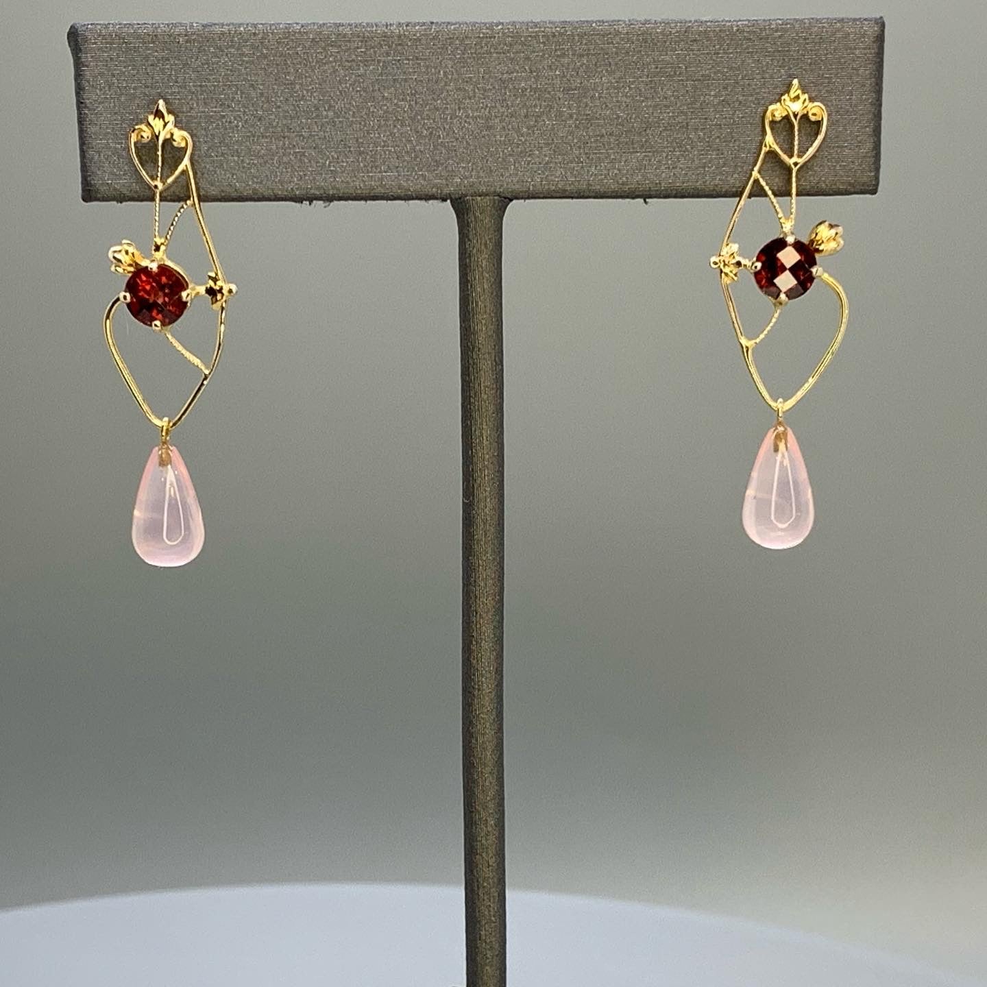 upcycled earrings featuring heart scroll motifs as well as alluding to the shape of a anatomical heart. Earrings have a heart filagree on top where the post is, and a 5mm round checkerboard cut orange/red garnet centered on earrings, and a rose quartz smooth briolette dangle.