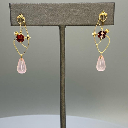 upcycled earrings featuring heart scroll motifs as well as alluding to the shape of a anatomical heart. Earrings have a heart filagree on top where the post is, and a 5mm round checkerboard cut orange/red garnet centered on earrings, and a rose quartz smooth briolette dangle.